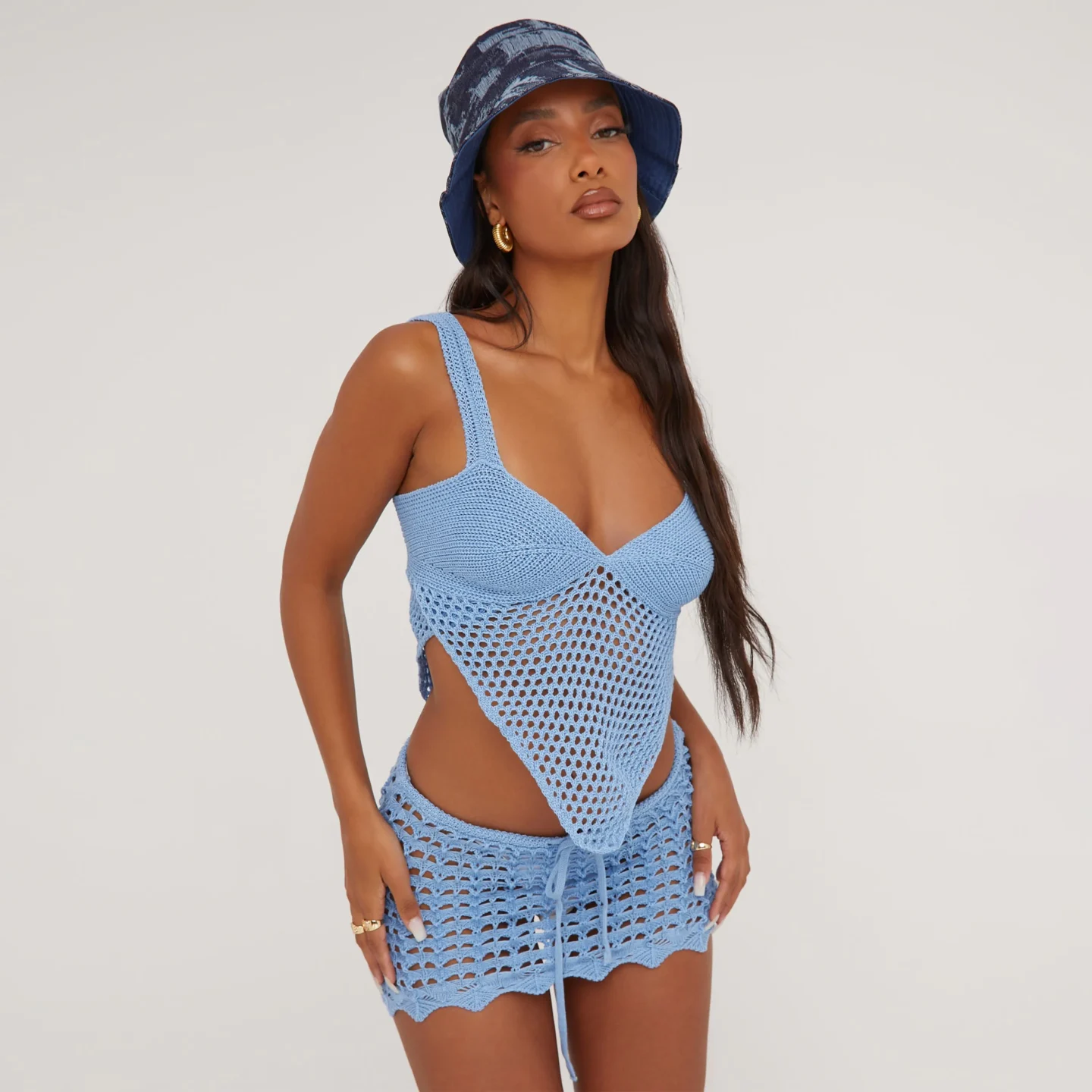 A blue crochet co-ord. The top is a bralet with thin straps, a v neckline and a draping v-front style. The skirt is a low rise mini skirt with a tie front waistband. 