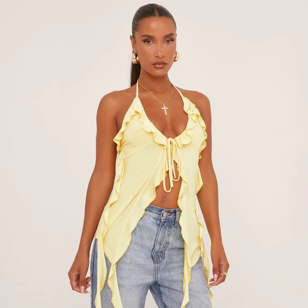 A yellow top with a plunge neckline and long frills that come off the top. It is a halterneck style that ties at the front with a bow. The woman wears it with blue jeans. 